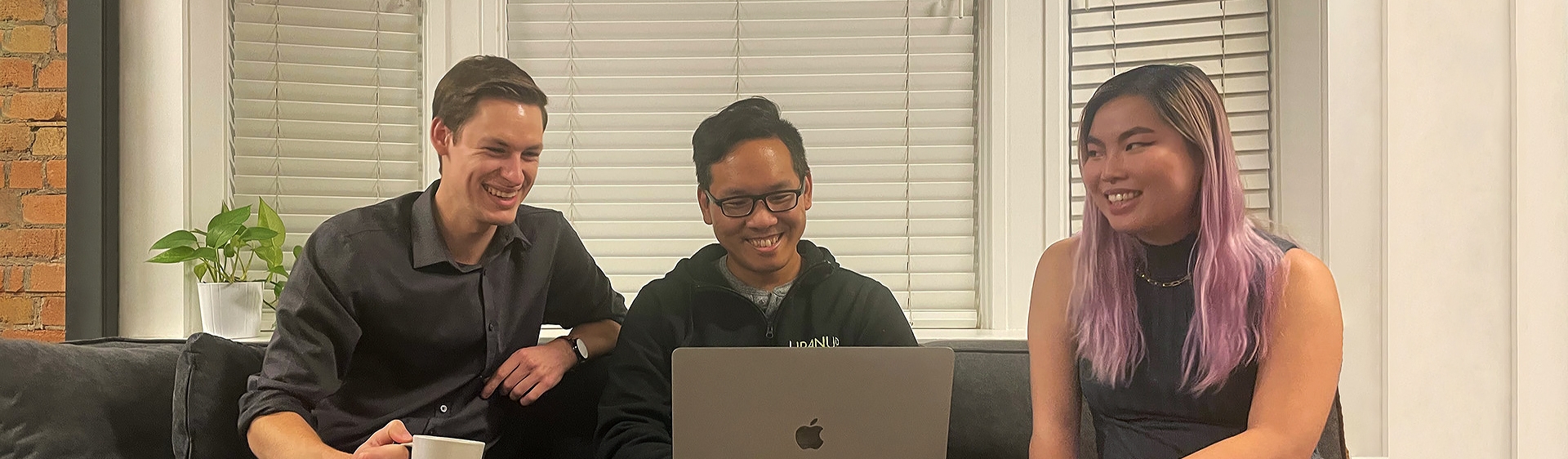 Two men and a woman looking at a laptop screen and smiling