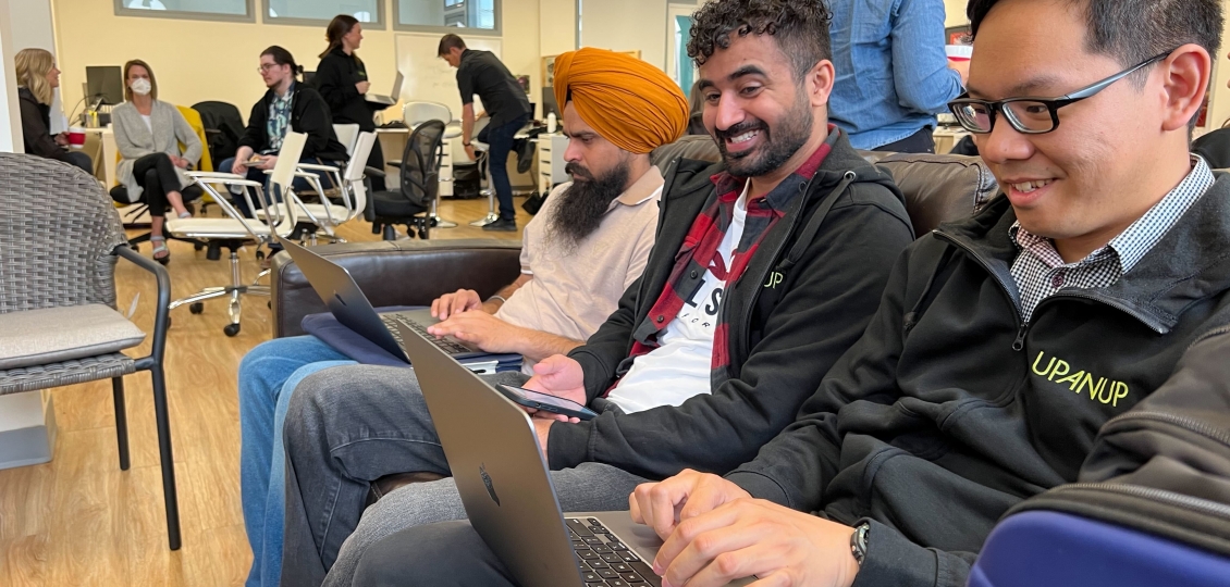 Three men sitting on a couch with laptops.