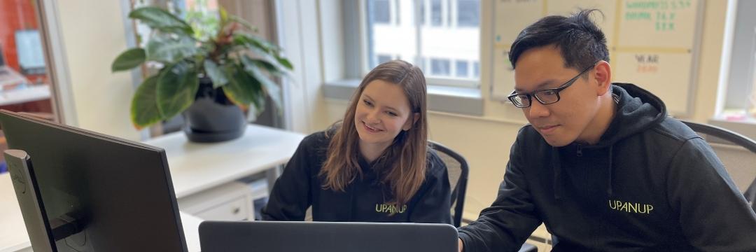 Two Upanup employees smiling while looking at their computer