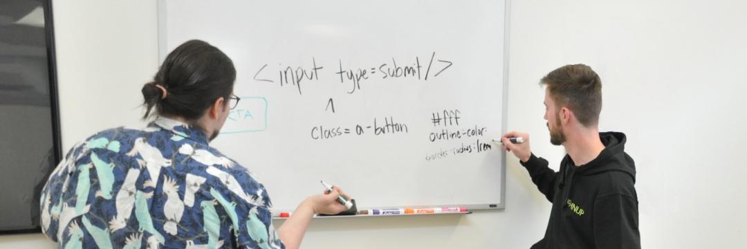 Upanup employee writing on a whiteboard teaching another employee about coding